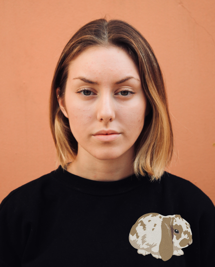 A young woman wearing a black crewneck sweatshirt with a tan and white rabbit embroidered on the left chest.